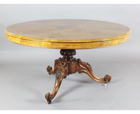 A Victorian burr walnut breakfast table, with circular tilt top, on floral carved tripod base and ceramic castors, Diam. 4ft 