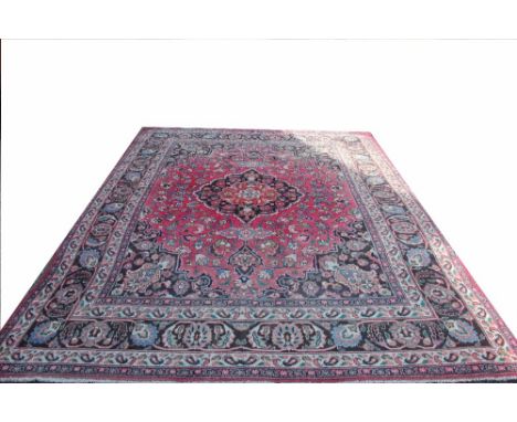 A Persian wool carpet, worked with an overall foliate design against a red ground, 343cm x 243cm