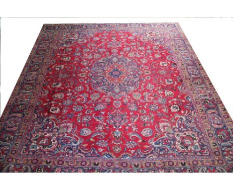 A Persian Kashan hand woven wool carpet, worked with a central floral panel and all over foliate design against a red ground,