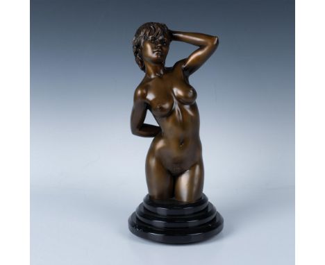 An erotic bronze sculpture in a golden-brass tone of a nude woman pushing her hair back from her face. The figure is placed o