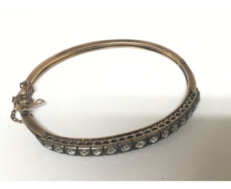 A gold bangle unmarked set with a row of fifteen graduating old cut diamonds. Total weight 10g