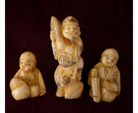 JAPANESE CARVED IVORY NETSUKE
of a man holding a fish, 5.2cm; an ivory netsuke of a man seated with an umbrella, 3cm high; an