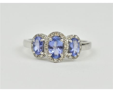 A 9ct white gold, diamond and tanzanite three stone ring, the three central stones with diamond accent halos, stamped to shan