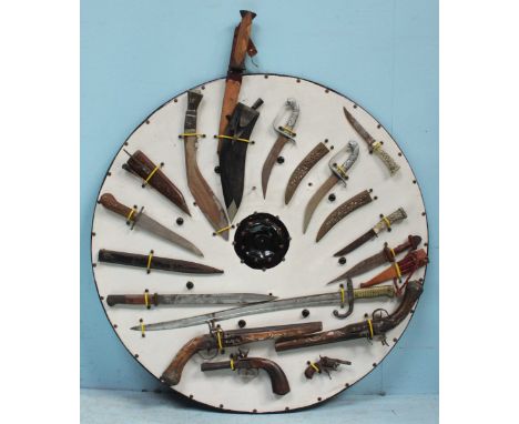 A collection of bayonets, dagger, knives and antique firearms mounted to a large circular wooden board, including a French M1