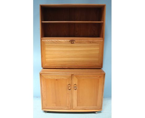 An Ercol light elm bookcase, the top section with adjustable shelf, above a hinged door opening to reveal further shelves, ov