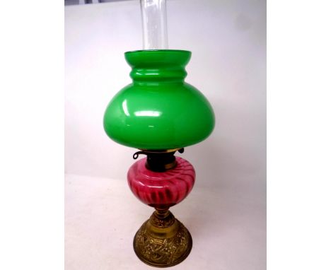 An antique brass duplex oil lamp with cranberry glass reservoir, chimney and green glass shade, height 50 cm 