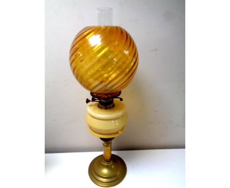 An antique brass oil lamp with glass reservoir, chimney and amber shade, height 65.5 cm  