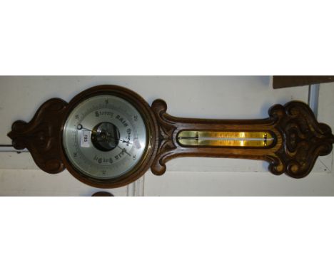 A carved oak aneroid wall barometer with brass thermometer.