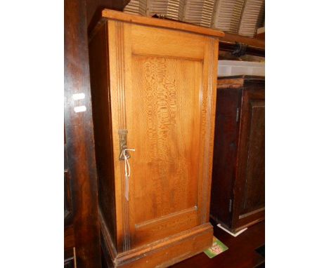 An Edwardian light oak bedside cupboard with shaped back, tram lined panel door and brass bell shaped handle, raised on a pli