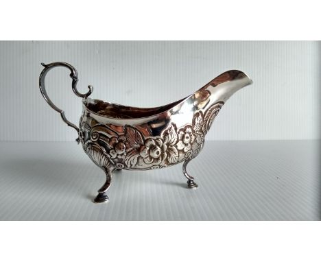 A George III Irish silver sauce boat of helmet form with embossed floral decoration, c-scroll handle on shell pad feet by Mat