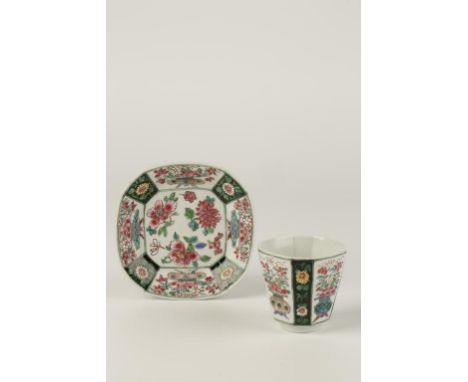 A CHINESE FAMILLE VERTE/NOIR CUP AND SAUCER decorated with panels containing jardinieres of flowers and blooms within conform