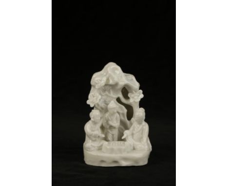 A CHINESE "BLANC DE CHINE" GROUP of three figures playing Go in the shade of rockwork over which climbs flowering shrubs, pro