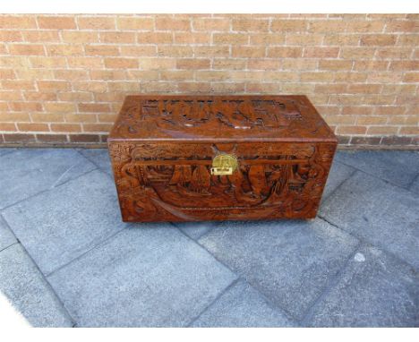 A CAMPHORWOOD TRUNK the lid and front carved with scenes of sailing boats flanked by serpents, 55cm high, 102cm wide, 51cm de