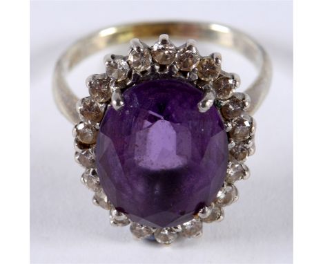 AN AMETHYST AND DIAMOND CLUSTER RING the white mount stamped '18ct', the oval cut, 13.6 by 10.6 by 7.8mm deep, enclosed by tw