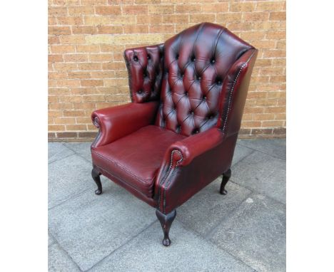 AN UPHOLSTERED RED LEATHER WING ARMCHAIR buttoned and studded and raised on four cabriole supports. 114cm high, 94cm wide and
