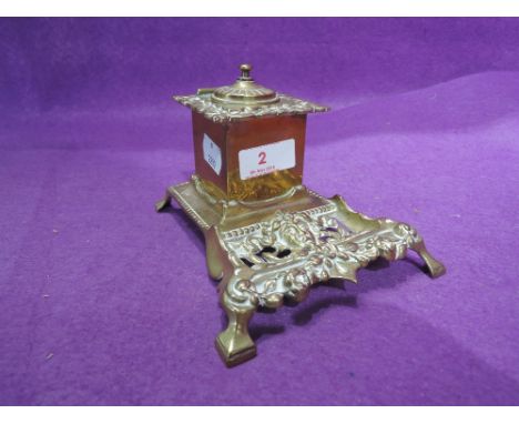 A vintage brass cast ink well with ornate decoration and ceramic inner fitment