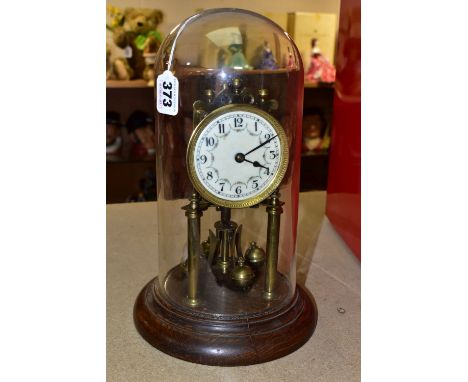 A GLASS DOMED ANNIVERSARY CLOCK, columns, crown and pendulum with brass application , wooden pedestal, pie crust bezel, cream