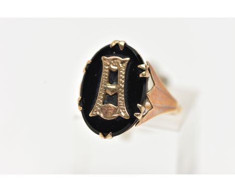 A YELLOW METAL INITIAL RING, an oval cut onyx centrally set with a yellow metal letter, prong set in yellow metal leading ont