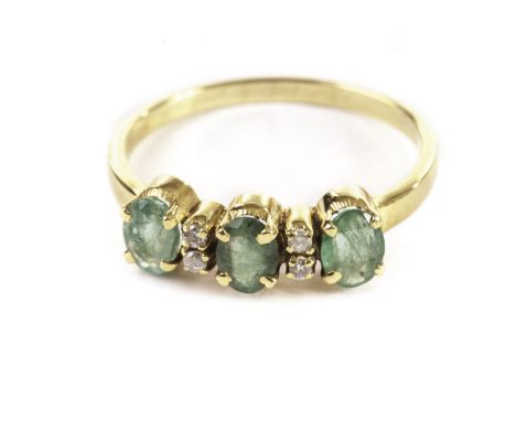 An emerald and diamond dress ring, having three oval green stones and a pair of brilliant cuts between them in yellow metal m