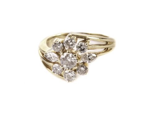 A modern diamond cluster ring, the crossover style yellow metal mount having a flower head style group of brilliant and marqu