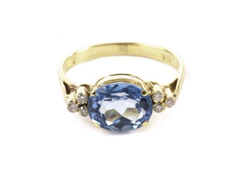 A modern gem set dress ring, having a bright blue oval stone, possibly a topaz, and two sets of three brilliant cuts to each 