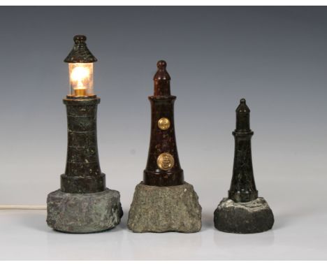 Three Cornish serpentine lighthouse models, on stone bases, one as a desk lamp (working) 26cm. high, together with one having
