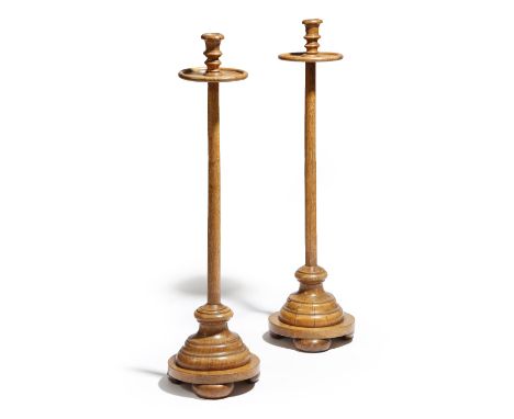 A pair of turned oak candlestands, each with an urn nozzle, above a dished drip-pan, late 19th century, 88cm high, 23.5cm wid