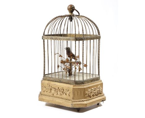 A late 19th century French brass musical automaton singing bird, perched on a bar in a birdcage, with leaf and floral decorat