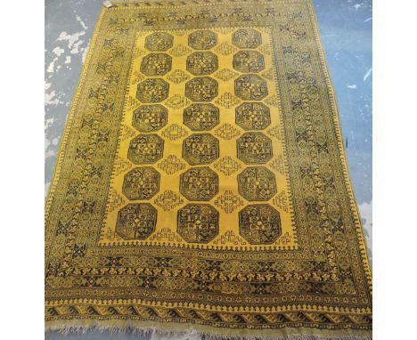 An Afghan gold ground small carpet woven with rows of octagonal devices within a wide multi border