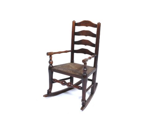 A 19TH CENTURY COUNTRY MADE CHILD'S ARMCHAIR with a ladder back and rush seat, turned supports and converted to a rocking cha