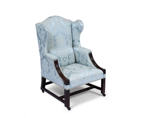 A MAHOGANY FRAMED GEORGIAN STYLE WING BACK ARMCHAIR upholstered in light blue material with acanthus leaf pattern, overstuffe
