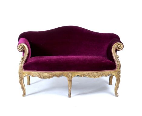A VICTORIAN CARVED WOOD GILT FRAMED SMALL CAMEL BACK SOFA upholstered in purple material, with scrolling arms and serpentine 