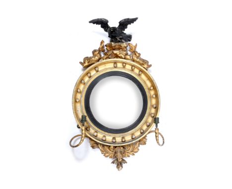A REGENCY GILT FRAMED CIRCULAR GIRANDOLE, the cresting carved with eagle and two dolphins, convex mirror plate and two candle