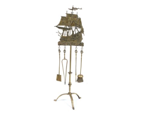 AN OLD CAST BRASS FIRE IRON STAND surmounted by a galleon setting sail, supporting the shovel, tongs, poker, brush and trivet