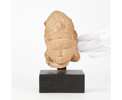 Carved sandstone head in the form of a female deity, India ca. 10th-12th centuries. With a wooden display base.(Head) Height: