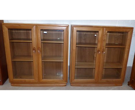 A pair of Ercol light elm display cabinets enclosed by two bevelled glass doors