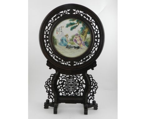 A Chinese circular porcelain plaque, depicting two figures playing chess, in a carved hardwood frame. H.54cm W.