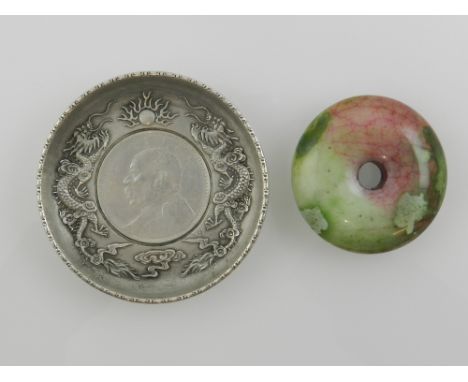 A Chinese white metal dish having a coin insert, together with a circular jade pendant. 