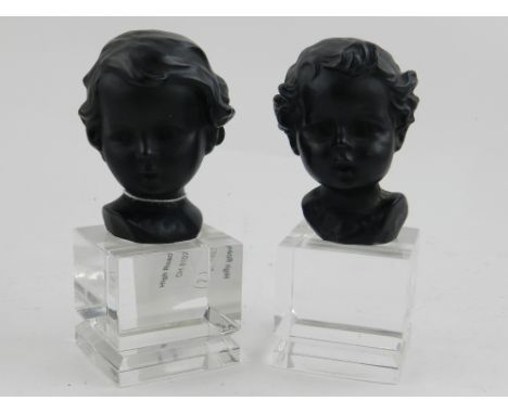 A pair of black glazed ceramic head and shoulder busts of children, mounted on a square glass plinth 