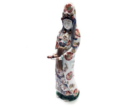 A Japanese porcelain figure of Guanyin, Meiji period, standing holding a scroll, wearing a cloak enamelled with mons and clou