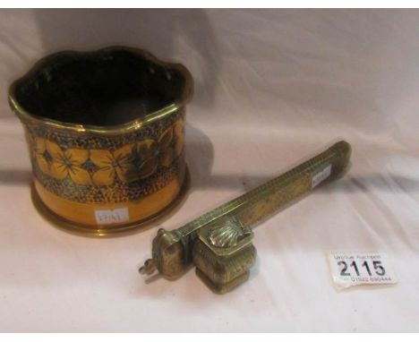 A heavy brass trench art bottle holder decorated with flowers and an ornate brass inkwell/pen case.