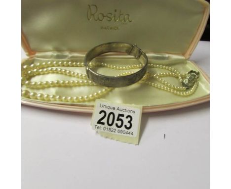 A double strand pearl necklace and a silver bangle.