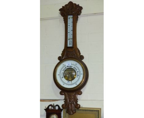 An Edwardian aneroid barometer with thermometer, in carved oak banjo case