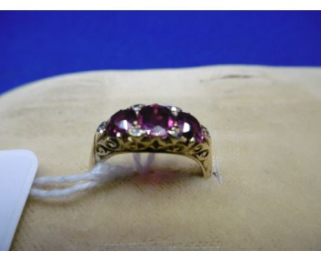 A THREE STONE RUBY AND DIAMOND YELLOW METAL RING, FLAW OR CHIP TO CENTRE STONE