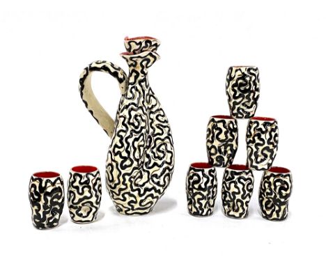A French Vallauris lidded liquor decanter, 23cmH, with eight small cups in a black and gilt design, 6.5cmH