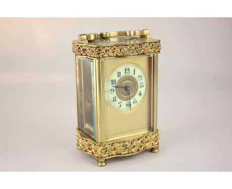 An ornate gilt brass and bevelled glass cased carriage clock with scrolling design and scalloped form, the circular enamel di