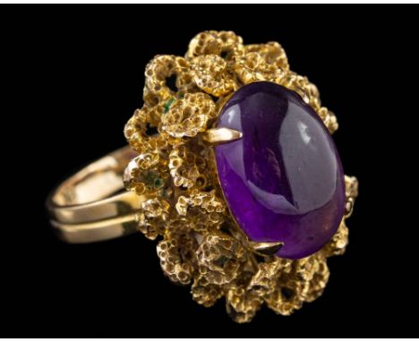 An amethyst dress ring,: the oval cabochon amethyst in a four claw setting, within a textured abstract surround, stamped 18K,