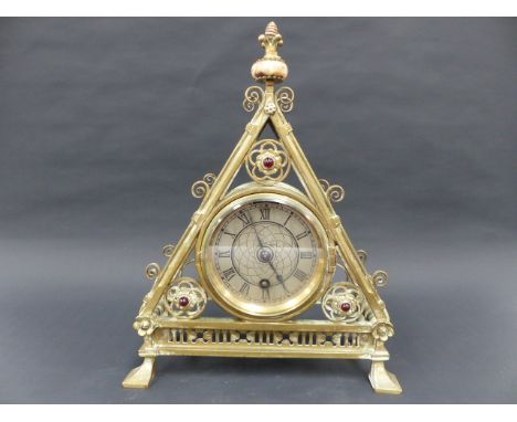 A VICTORIAN BRASS GOTHIC REVIVAL MANTLE CLOCK DESIGNED BY BRUCE TALBERT, TRIANGULAR FORM WITH CENTRAL DIAL, INSET RED CABUCHO