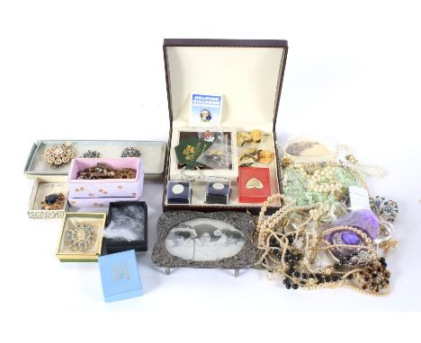 An assortment of costume jewellery. Including synthetic pearl necklaces, brooches, a silver plated photo frame, a white metal