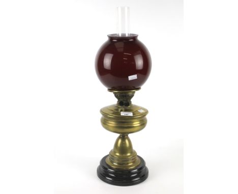 A Victorian brass oil lamp. With red glass globe shade, on a circular ceramic base. H58cm 